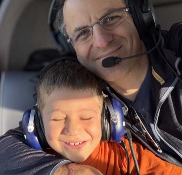 Allon Mason in a cockpit with one of his children, both wearing headsets.